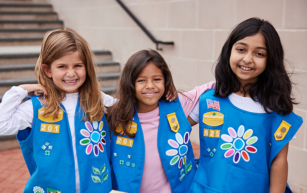 Three Daisy Girl Scouts with their arms around each other and smiling