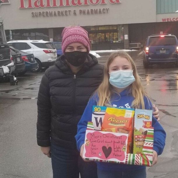 Adult standing with a girl who is holding a donation box filled with food