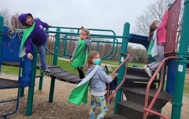Girl Scouts from troop 113 wearing superhero capes on a jungle gym