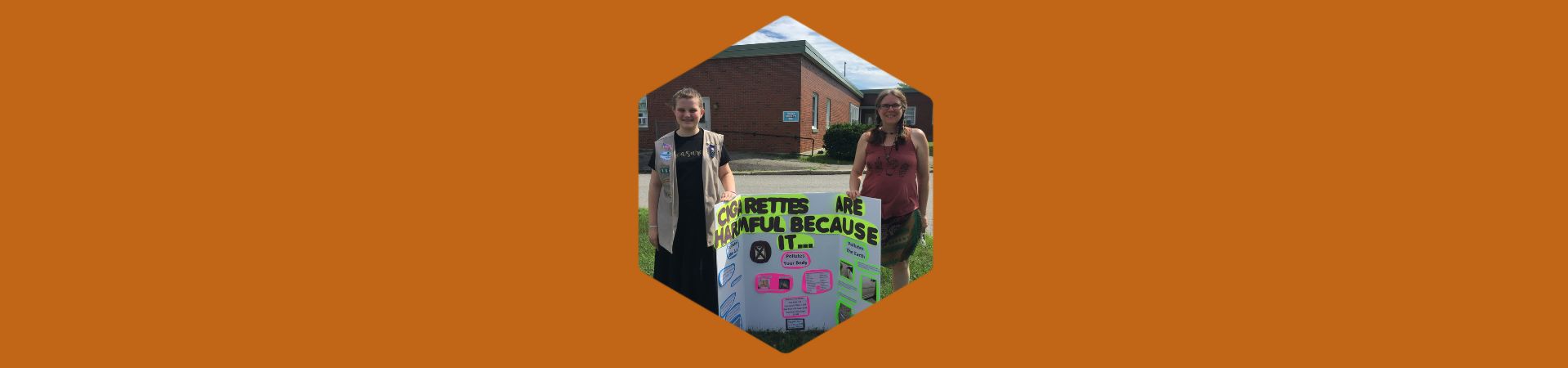  Two girls from troop 1340 standing on either side of a sign that explains why cigarettes are harmful 