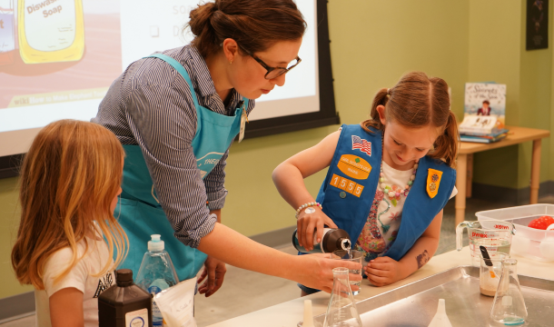 volunteer helping girl scouts with an experiment