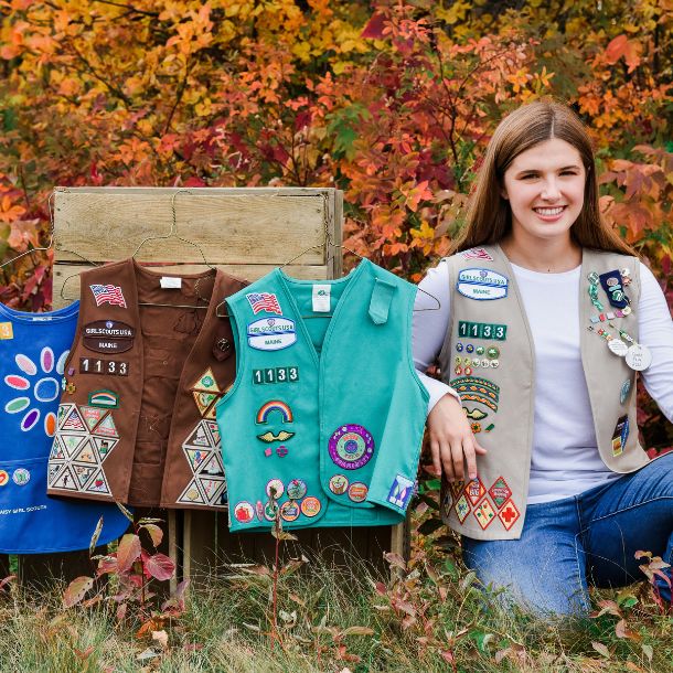 Picture of Madelyn sitting next to her Daisy, Brownie, and Junior vests